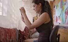 A woman sitting, working on fabricating a huge modern tapestry