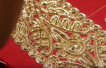 A close up of gold threaded ari embroidery on red fabric