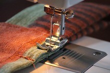 Close up photo of a sewing machine foot sewing fabric into a scrappy quilt